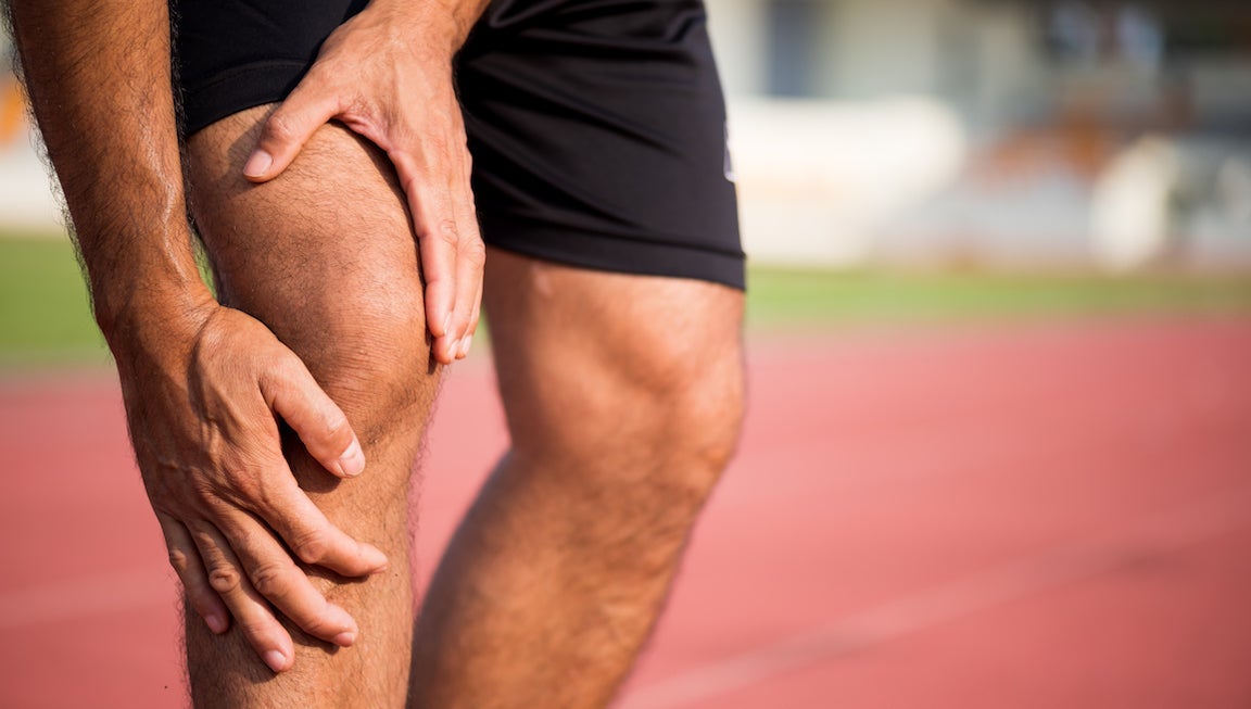 Man touching sore knee on a track.