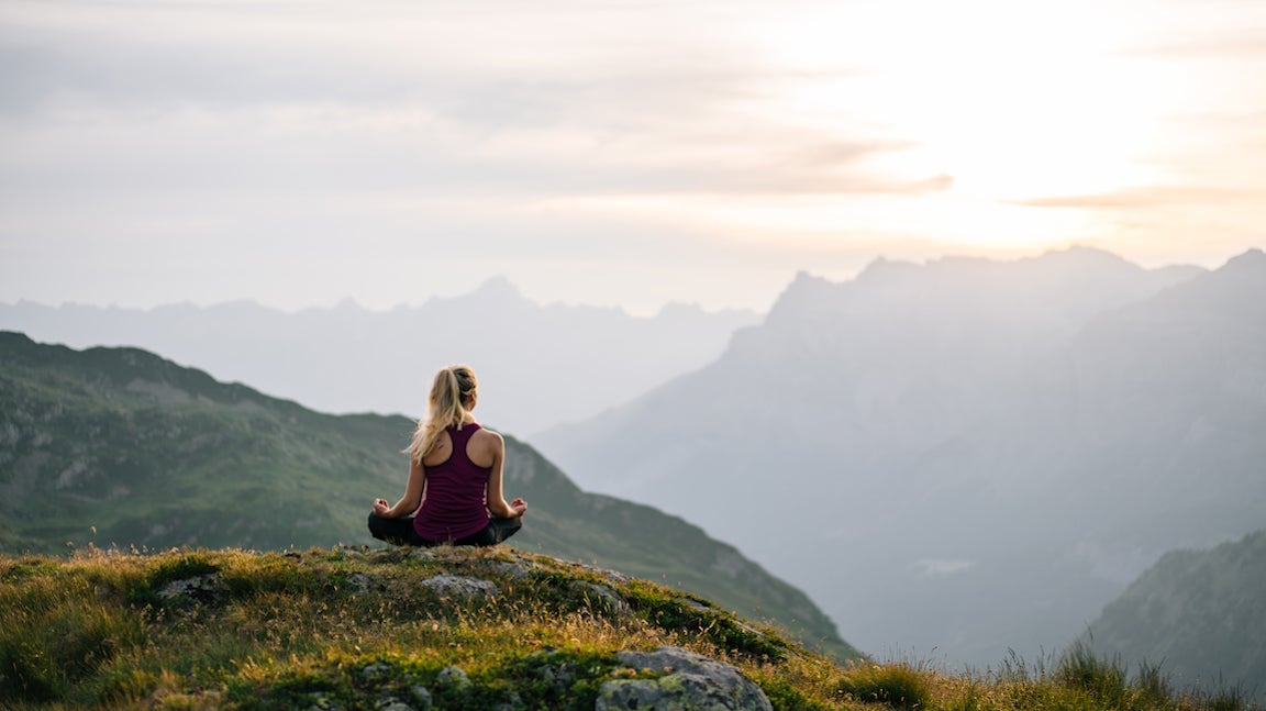 Women sits in lotus pose now capped mountains distant.