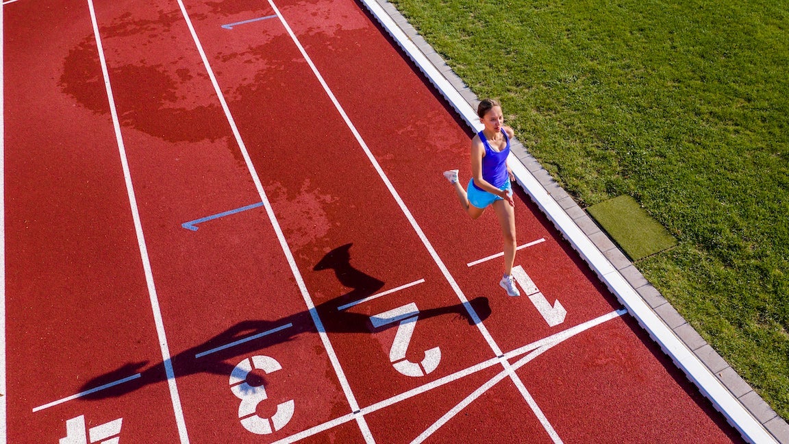 Aerial view of a female runner/athlete on a tartan track crossing finishing line.