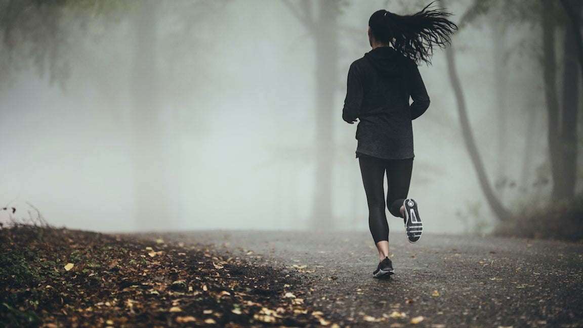 Rear view of female athlete jogging in foggy Autumn forest.