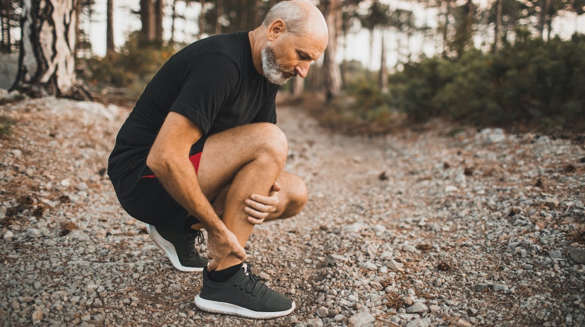 Senior man holding ankle by hands looking like he's in pain.