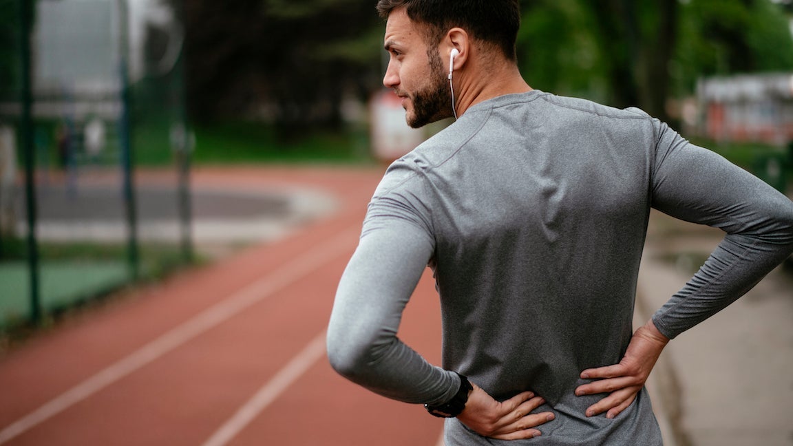 Runner suffering from backache at an outdoor track.
