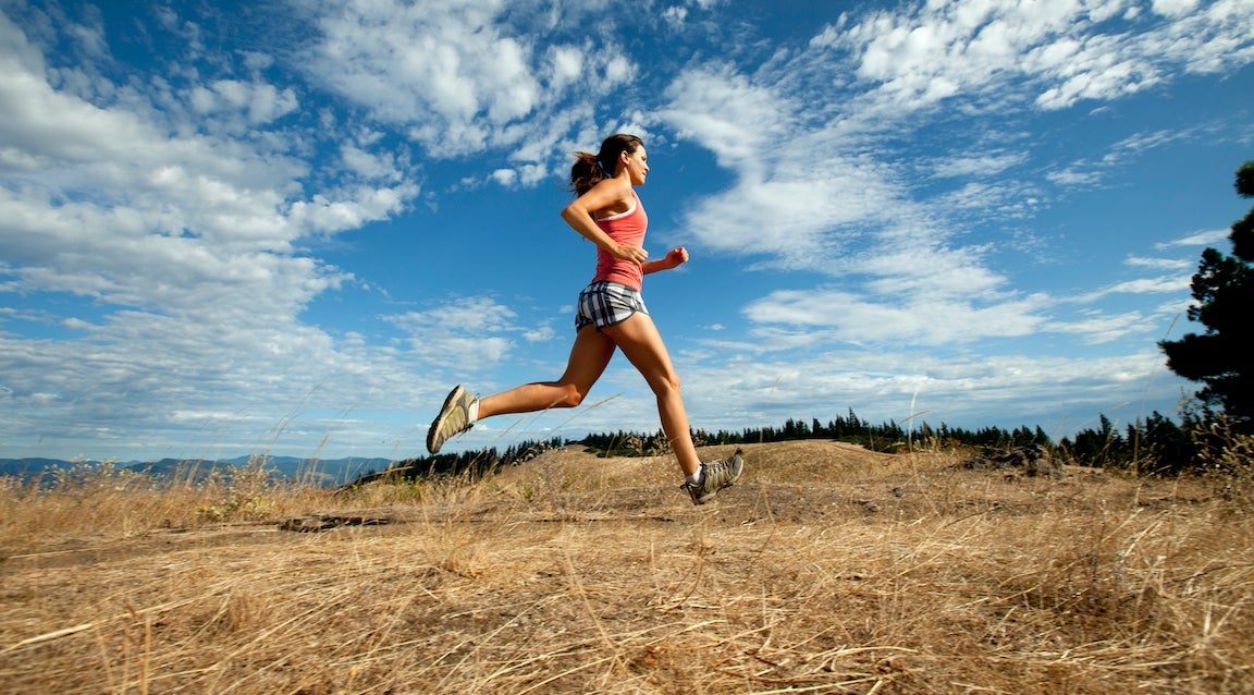 A woman trail running on a blue sky day with dramatic clouds.