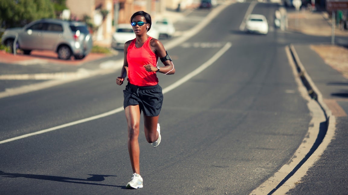 Woman running in sunglasses down a street in hot weather.