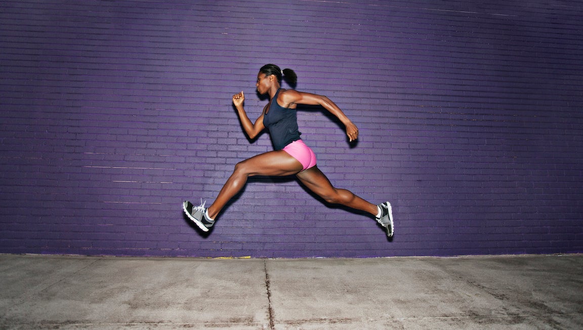 Female athlete running on sidewalk against purple wall.