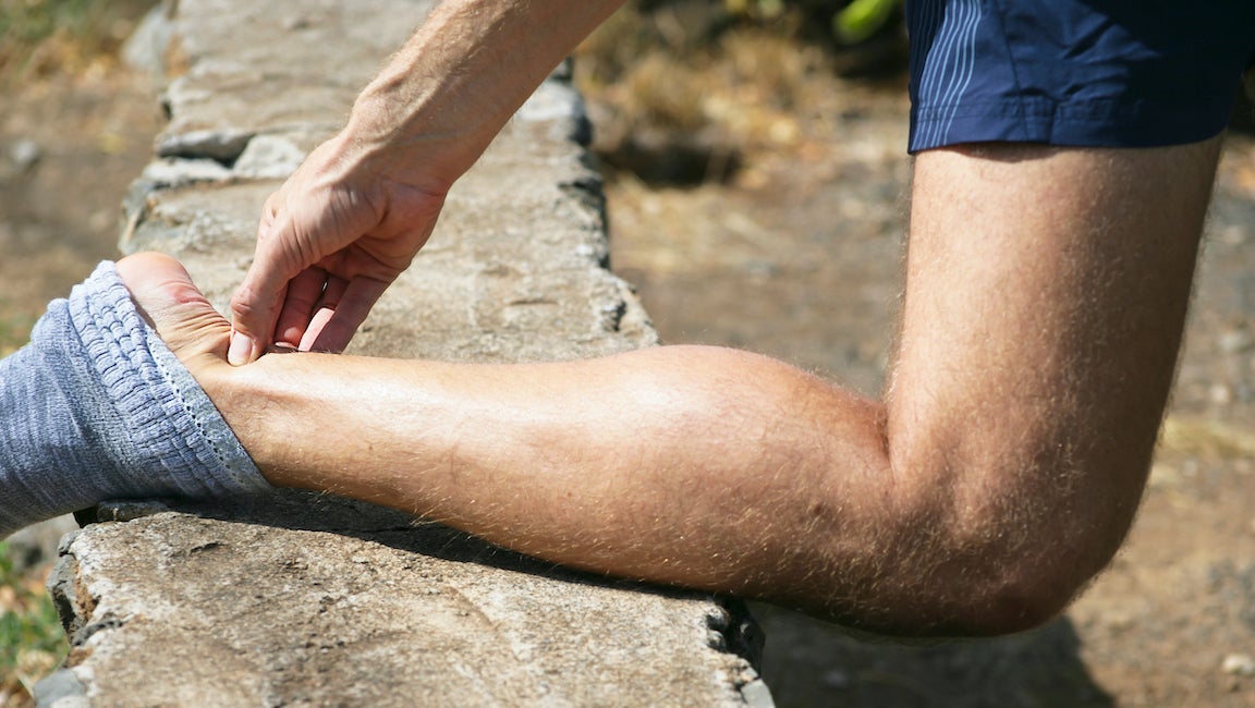 Man squeezing sore achilles while out running.