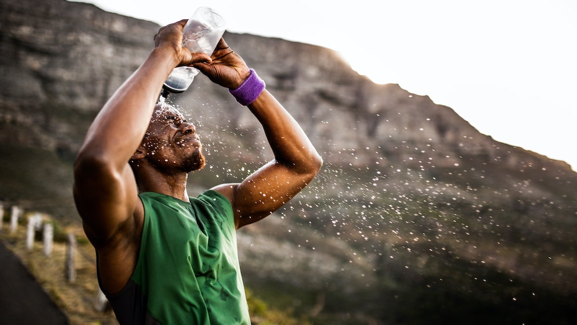 Athlete splashing himself with water from his water bottle after a hard run.