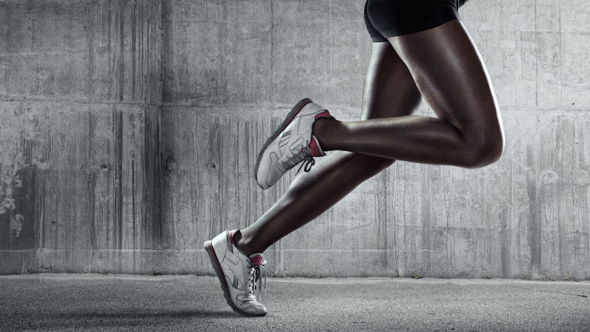 A low angle close up view of a female runners legs and feet running on concrete.