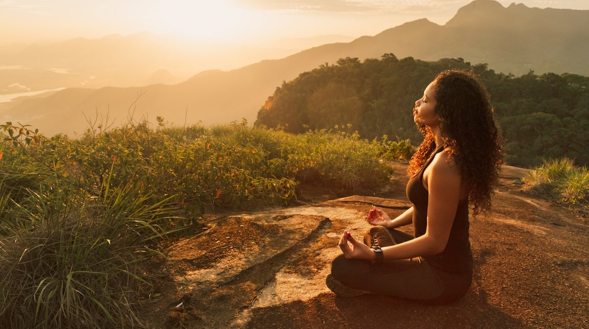 Young woman meditating on mountain top.