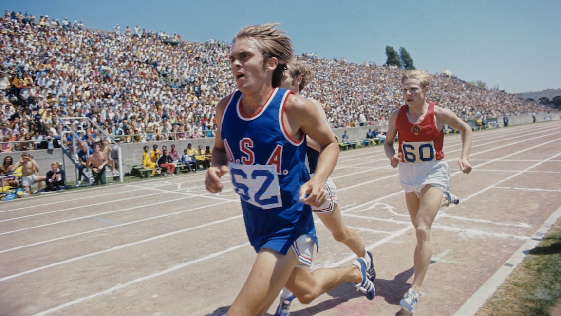 Steve Prefontaine racing in a blue uniform with a red USA on chest.