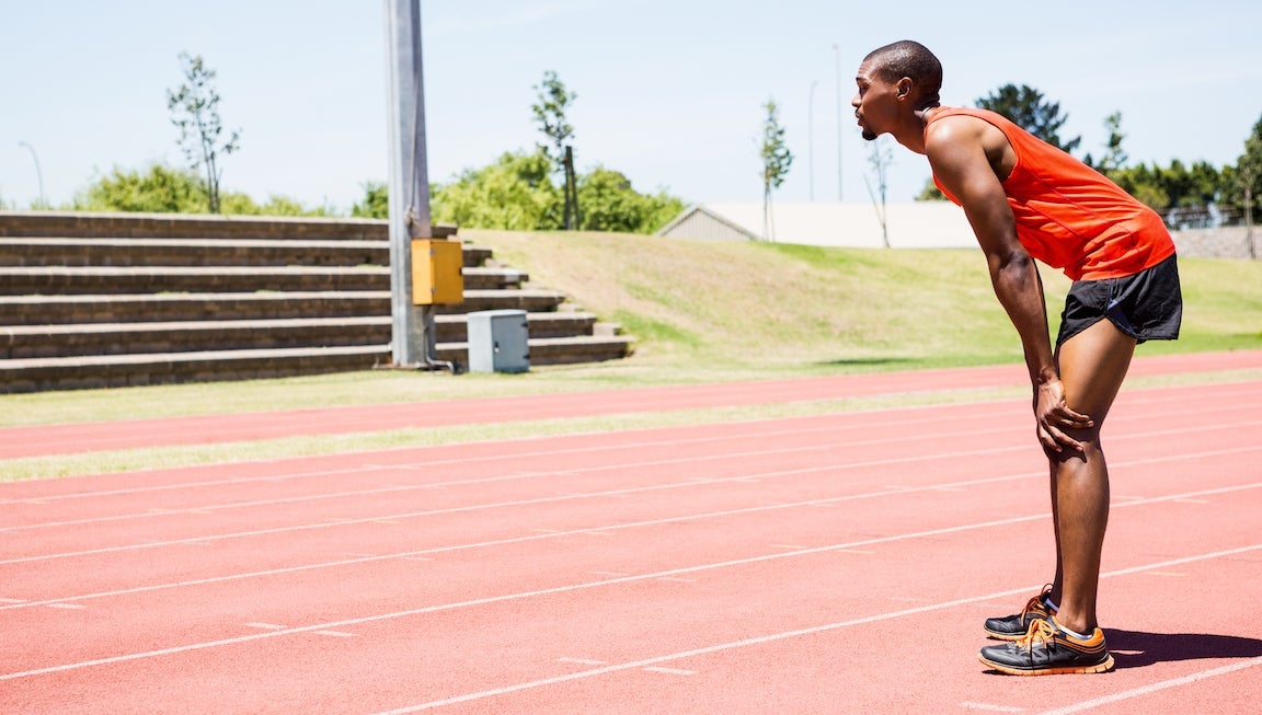 Tired athlete standing on running track on a sunny day.