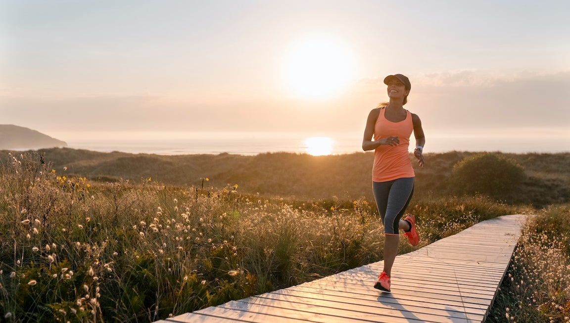 Athletic woman running along a coastal path at sunset.