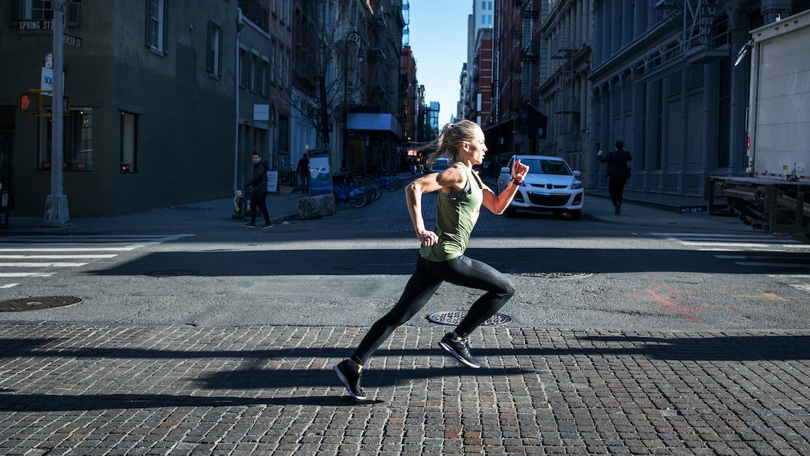 Side view of female athlete running on city street during sunny day in NYC.
