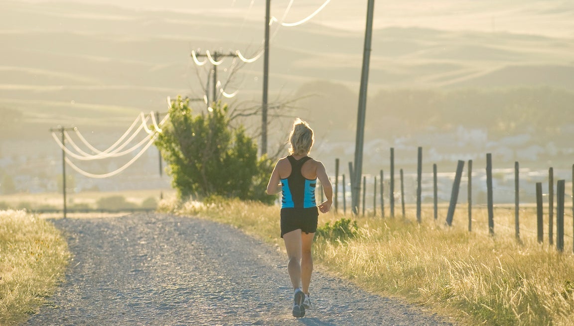 Woman running on road past telephone poles, rear view.