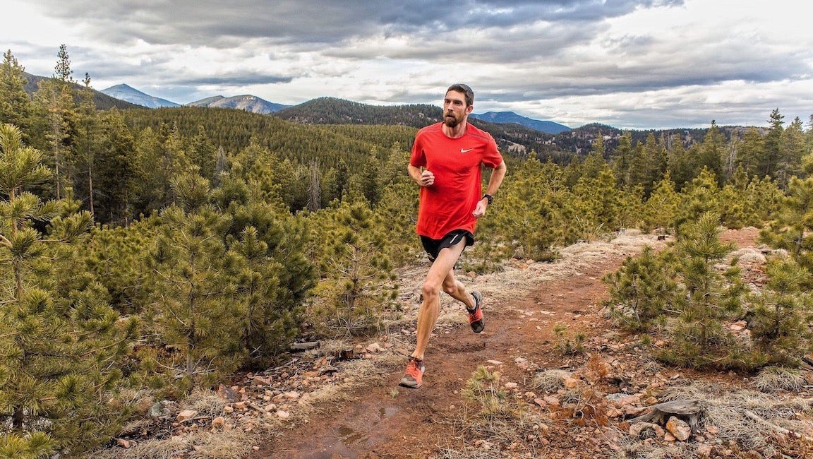 Man in bright red shirt running in the mountains.