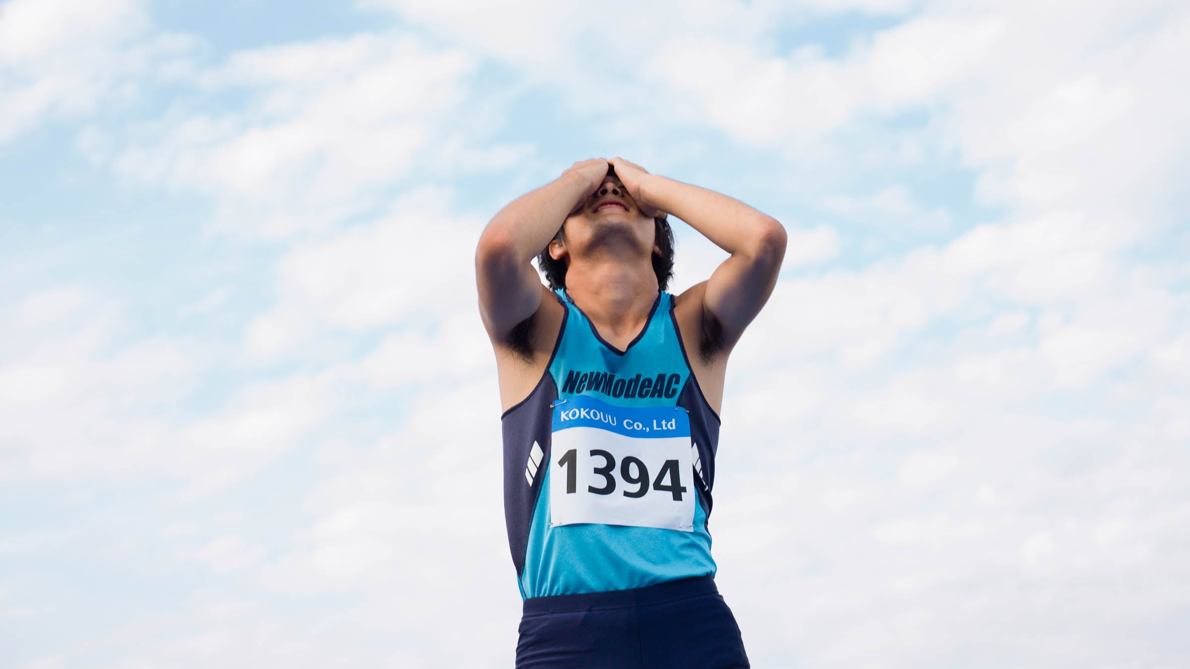 Runner with his hands to his face in anguish in front of a cloudy sky
