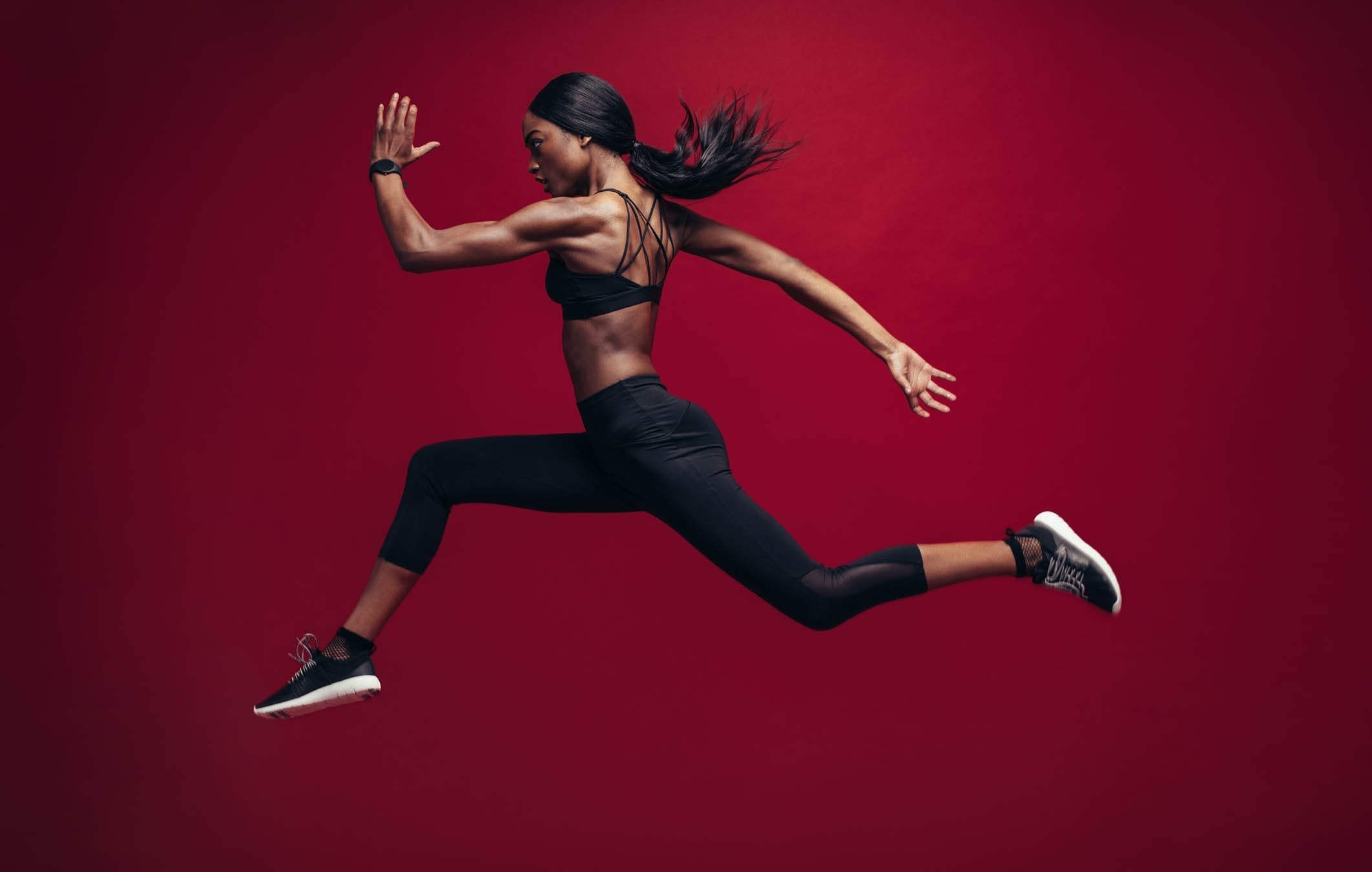 Female athlete running and jumping against red background.