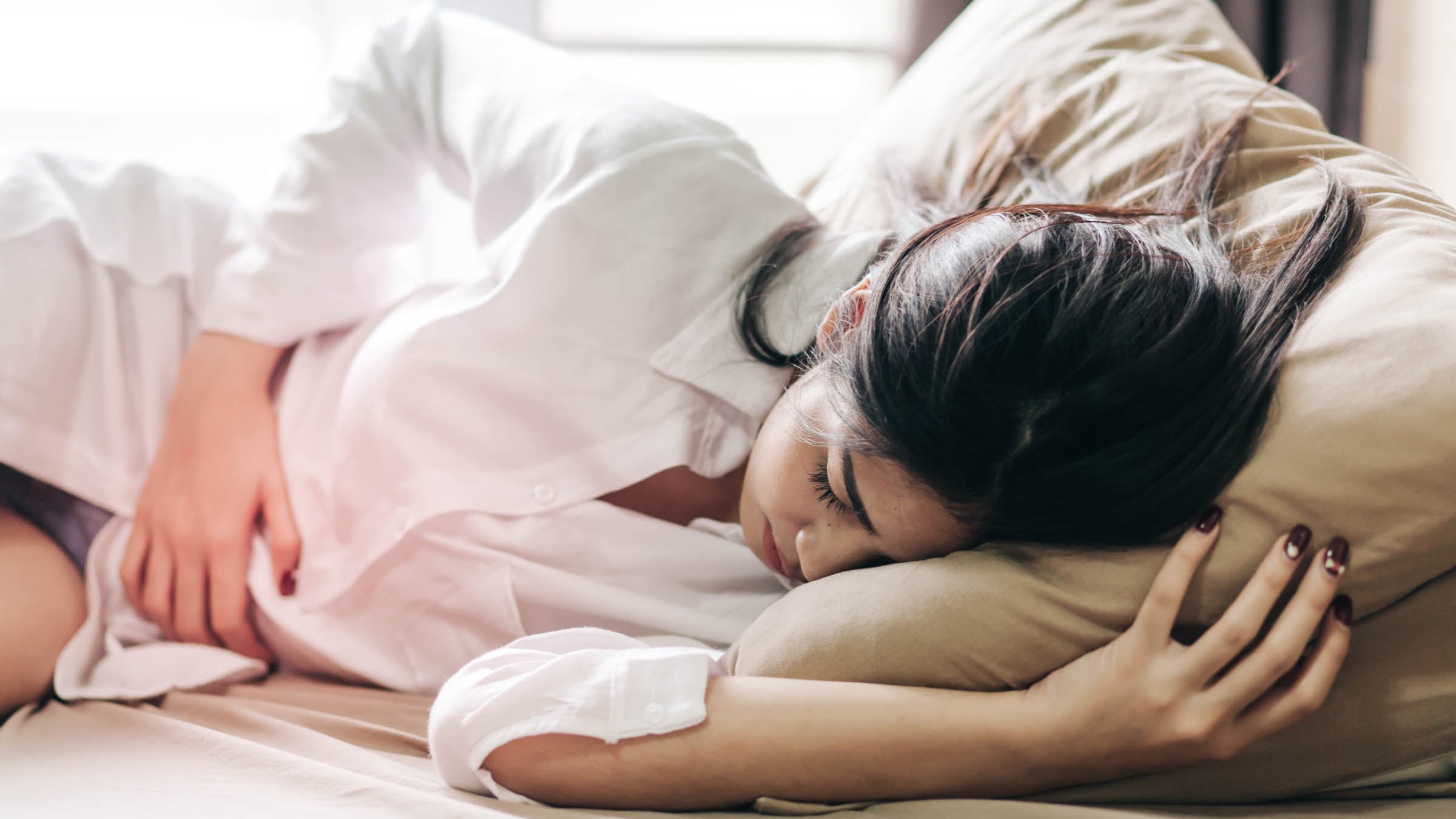 Woman Touching Abdomen While Sleeping On Bed At Home