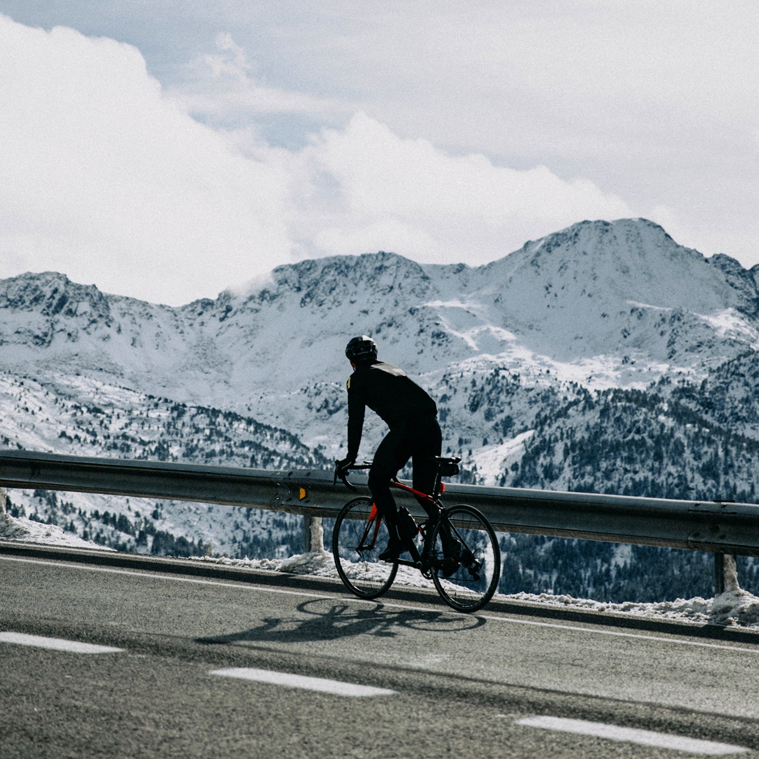 cyclist on mountain road with snowy mountains in the background