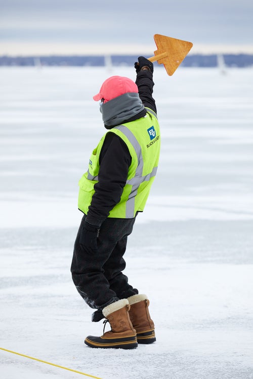 An official indicates the wind direction while coordinating with other officials to set the starting line.