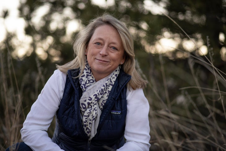 20181211_KHostetter_Dec2018_Albanese_1577 Woman with long blonde hair, white shirt, navy blue vest and scarf smiling, in field with tall grasses