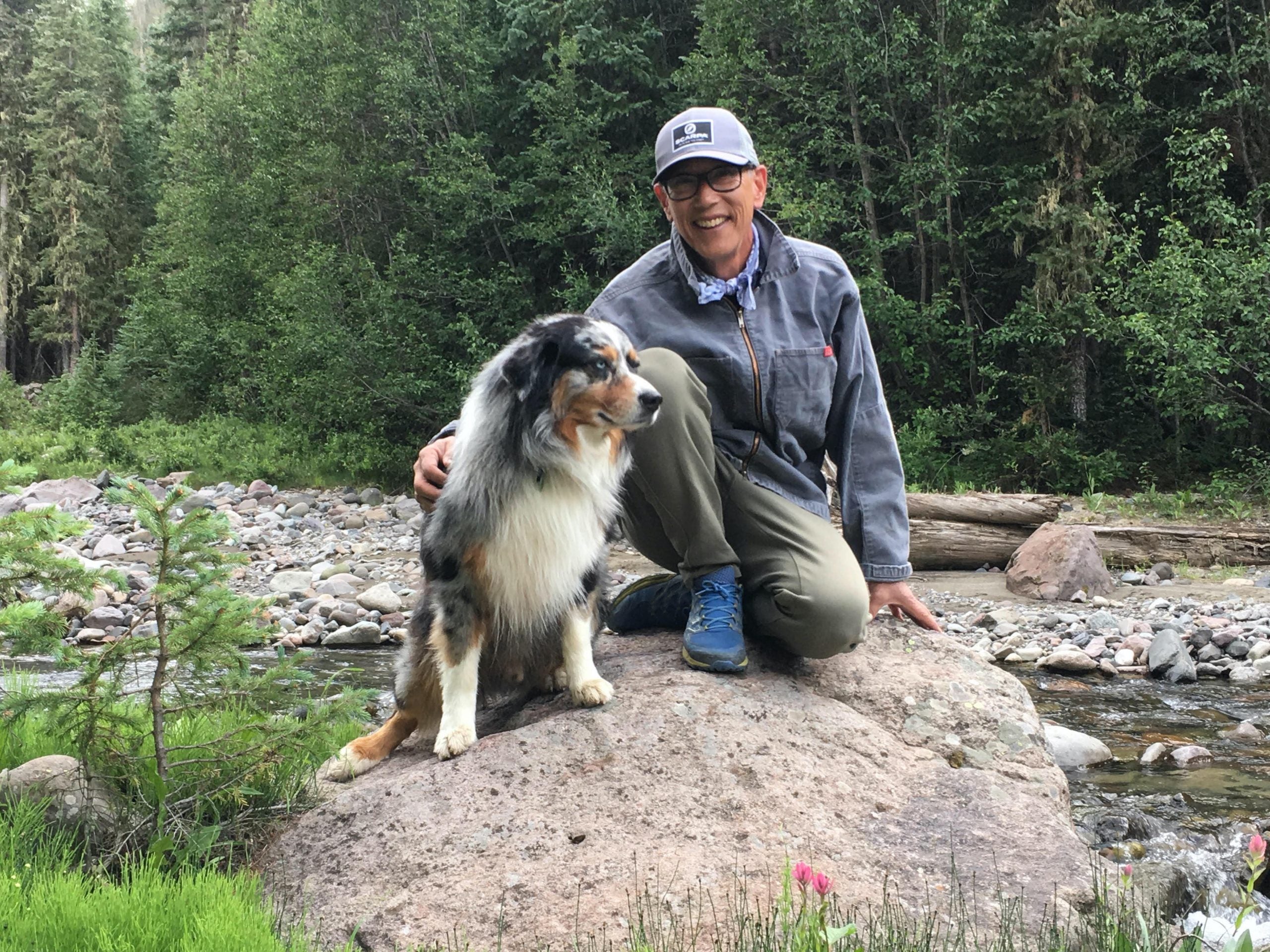 Kim Miller kneeling on a rock with his dog in front of a river