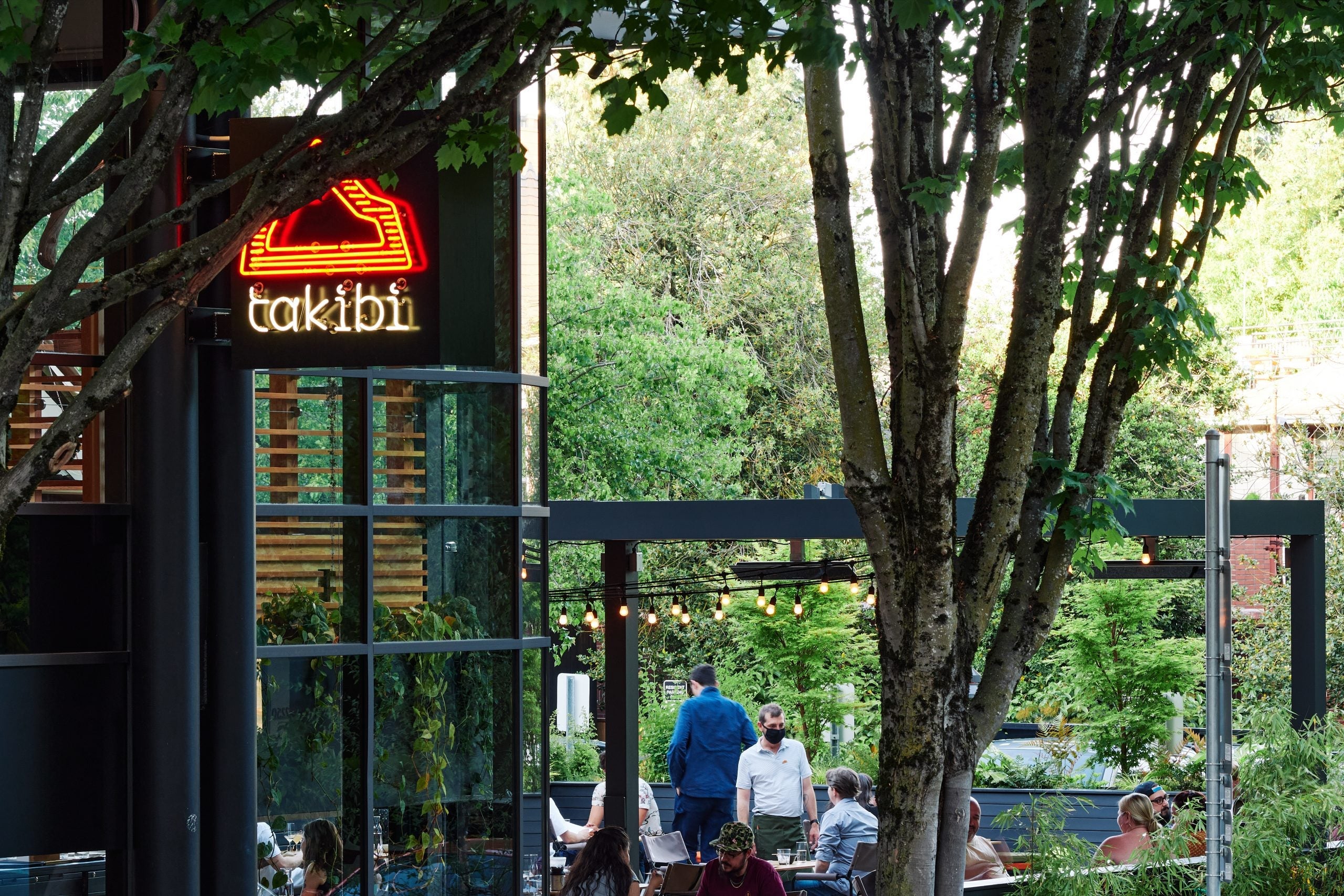 Exterior shot of Snow Peak's takibi restaurant with orange neon sign and trees