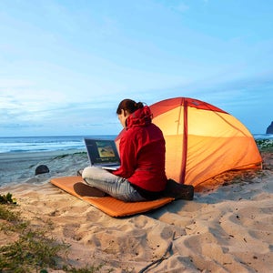 Woman using laptop at tent on the beach at dusk
