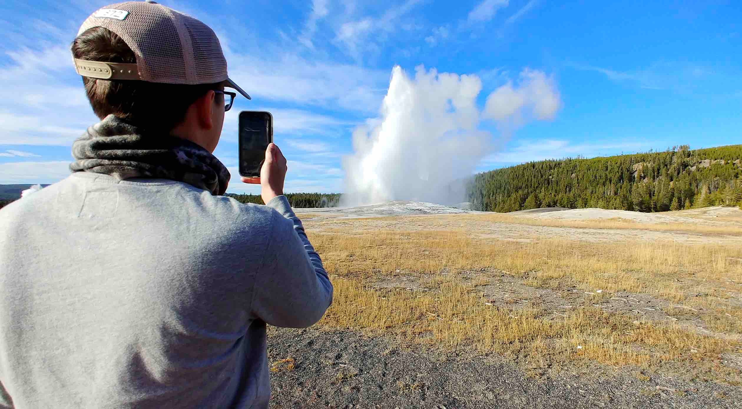 Man photographing Old Faithful in Yellowstone National Park with cell phone camera