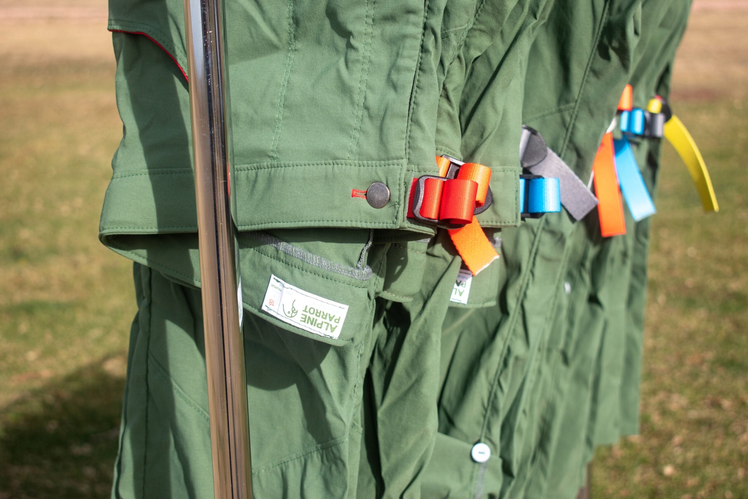 Green Alpine Parrot hiking pants hang on a clothing rack; plus-size outdoor apparel