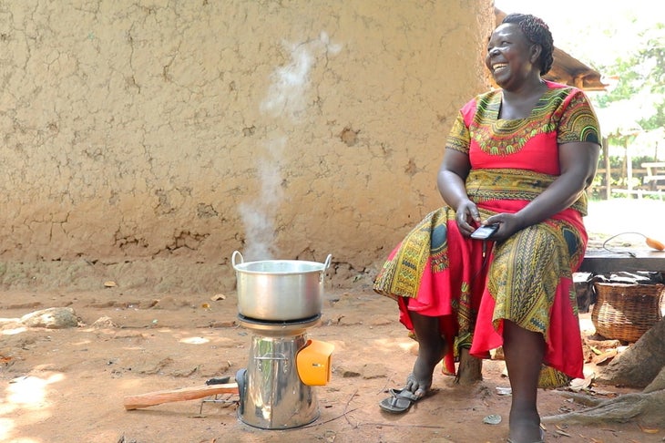 biolite HomeStove2_lifestyle1 Kenyan woman in red and gold dress boiling water and charging her mobile phone with a BioLite HomeStove.