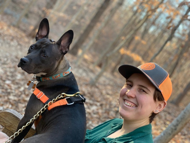 emmy johnson Emmy Johnson wearing green shirt and orange and gray hat with dog in the woods