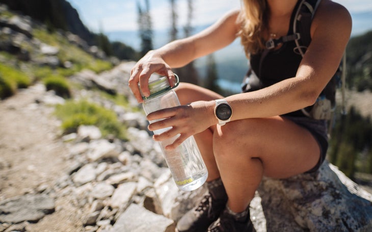 HP_Recon_5982 Woman sitting on rock holding clear plastic HydraPak water bottle.