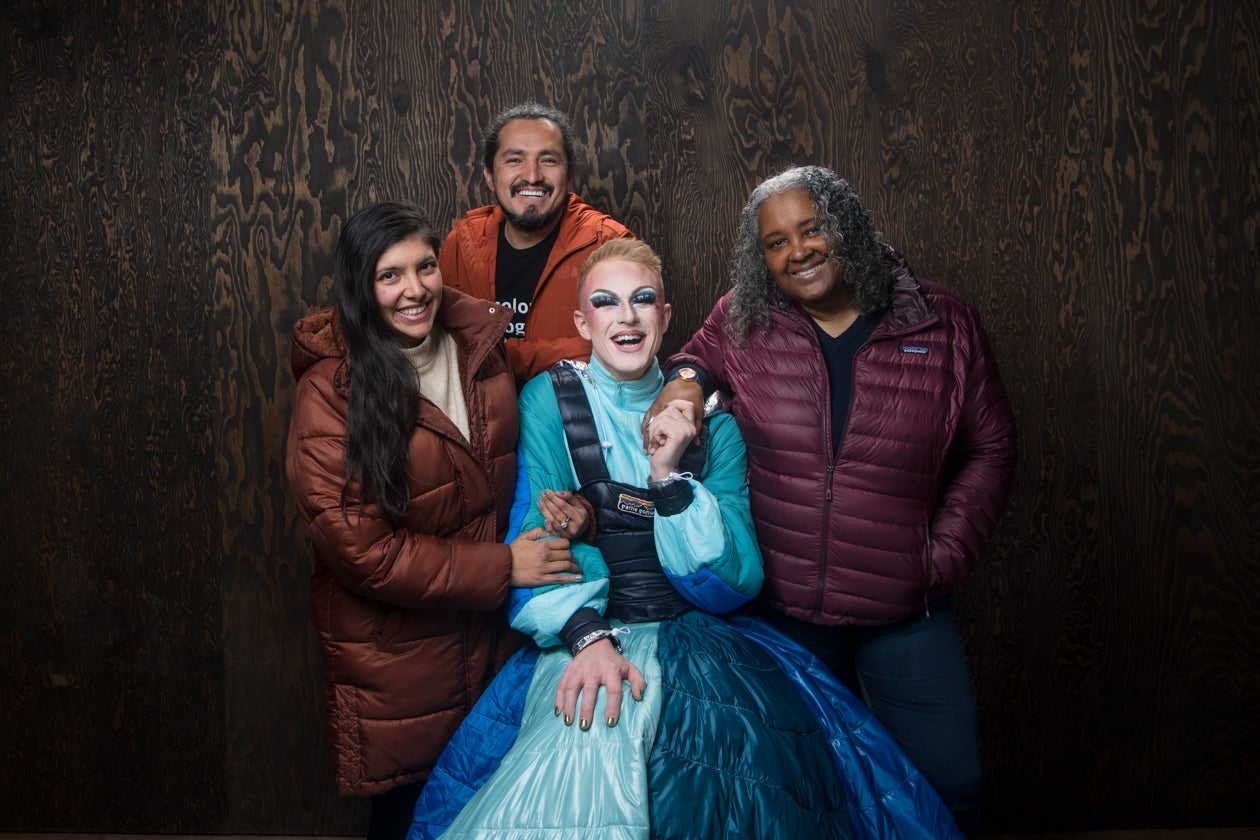 four people posing in front of brown background