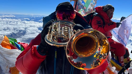 A climber plays a trumpet atop Mount Everest.