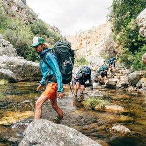 a group of hikers hike down a mountain stream carrying backpacks outdoors