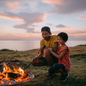 Father and daughter enjoying campfire at campsite at sunset