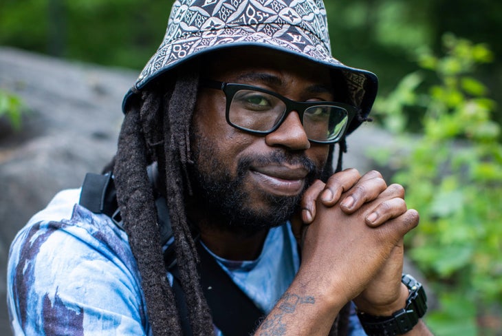 Malik Martin in a hat and glasses sits outside