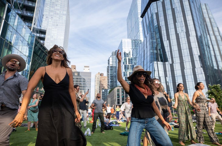 A crowd of people laugh and dance in a park in New York City