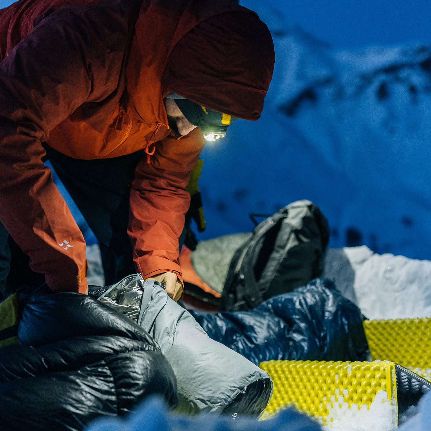 Winter camper with a headlamp unpacks Rab camping gear
