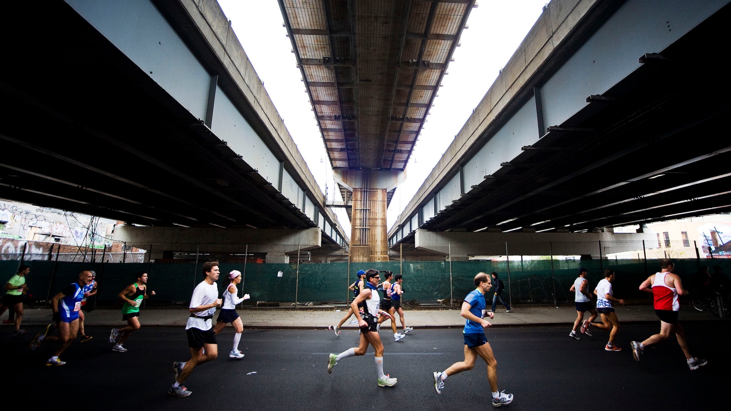 several runners of the NYC marathon run left to right under a shadowy tunnel