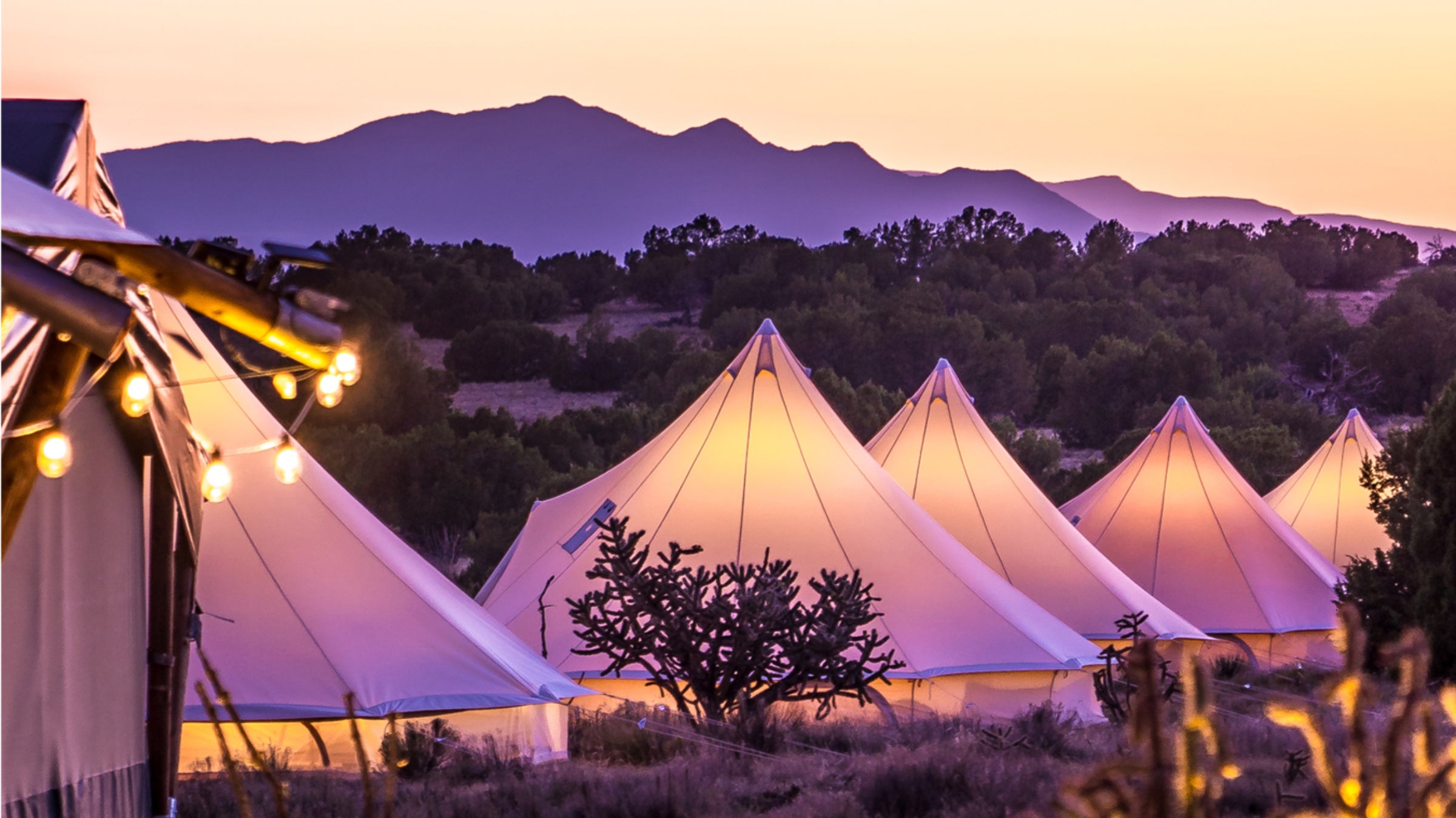 KitFox at dusk, with the tents aglow from the inside and the purple Sangre de Cristo Mountains in the distance