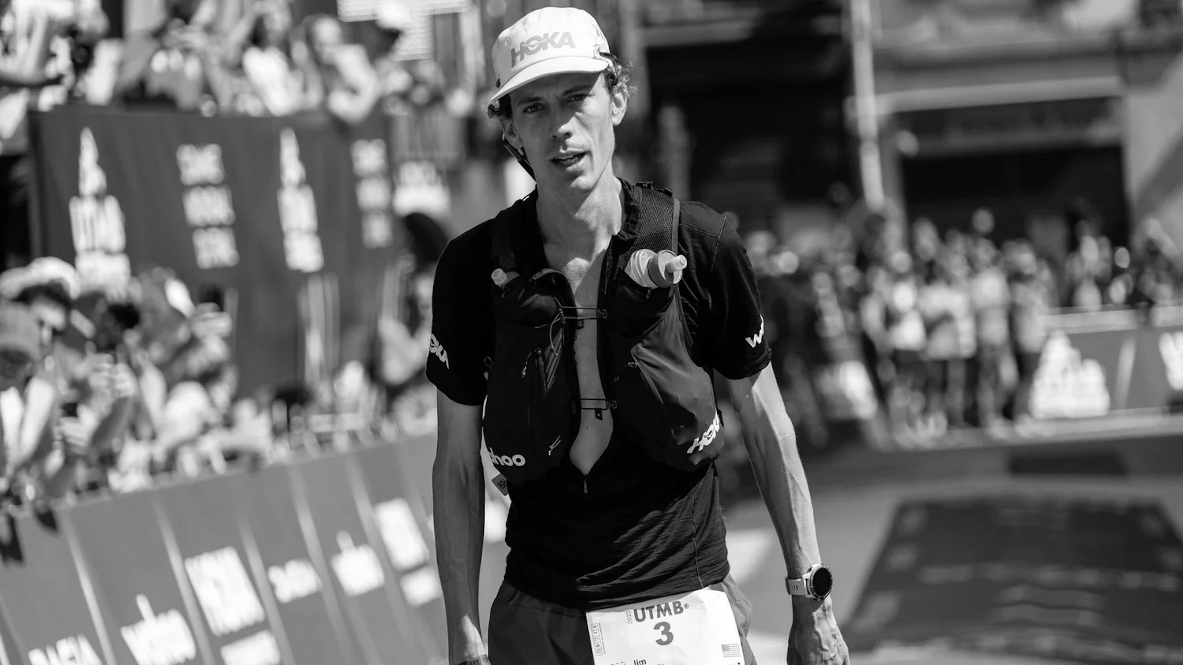 A runner in a white hat and black shirt at the finish line of a 100 mile race