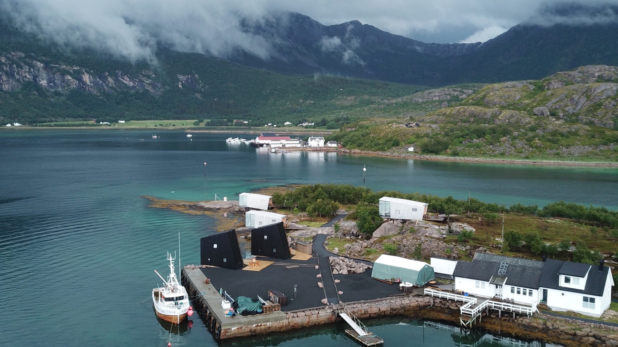 The island of Manshausen, surrounded by a boat and turquoise waters, with cloud-covered mountains in the background