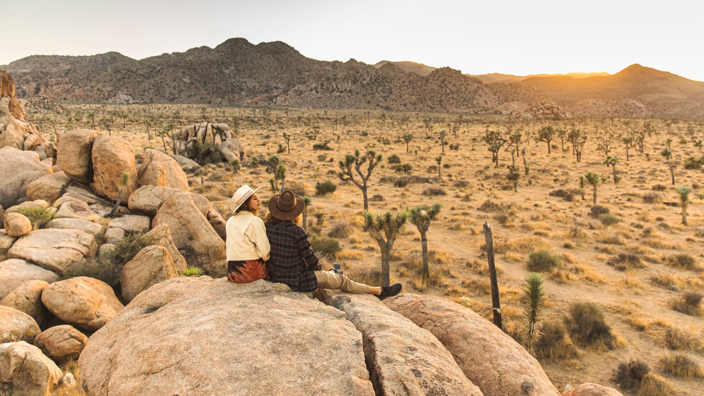 Two women sitting atop huge boulders, watching the sunset at Joshua Tree National Park, California.