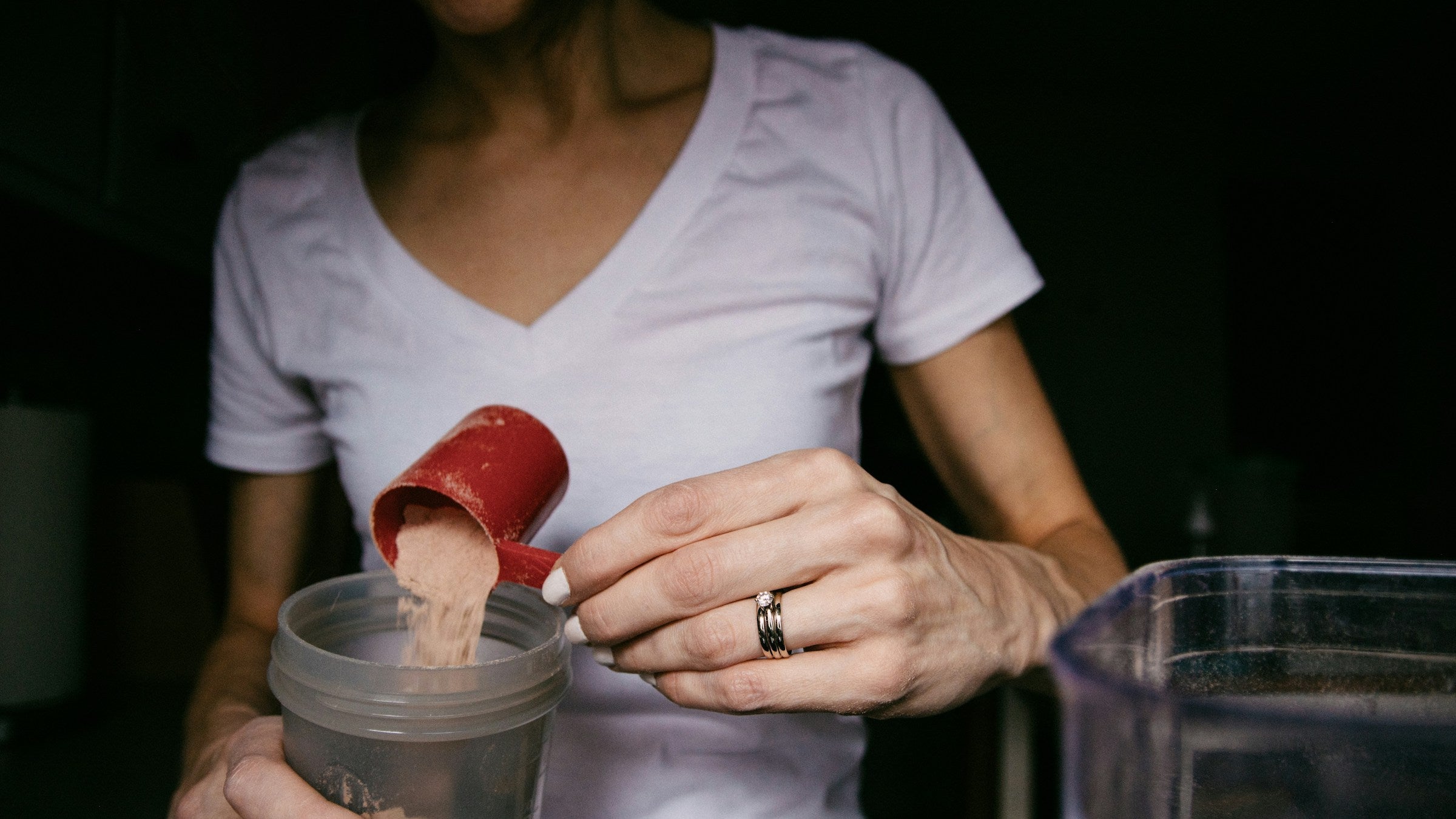 A woman pours protein powder into a protein shaker bottle