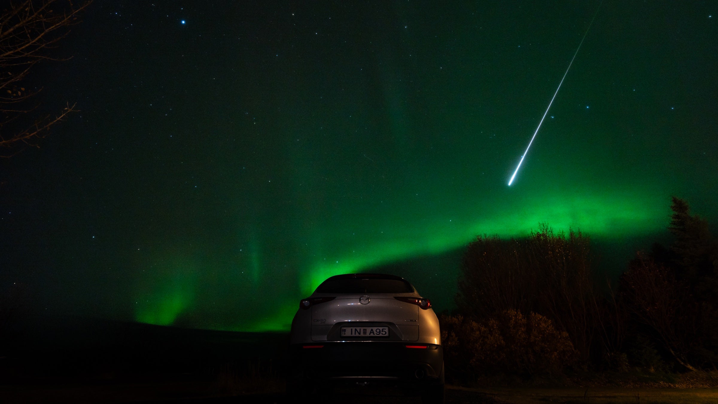 fireball streaking across green night sky over car