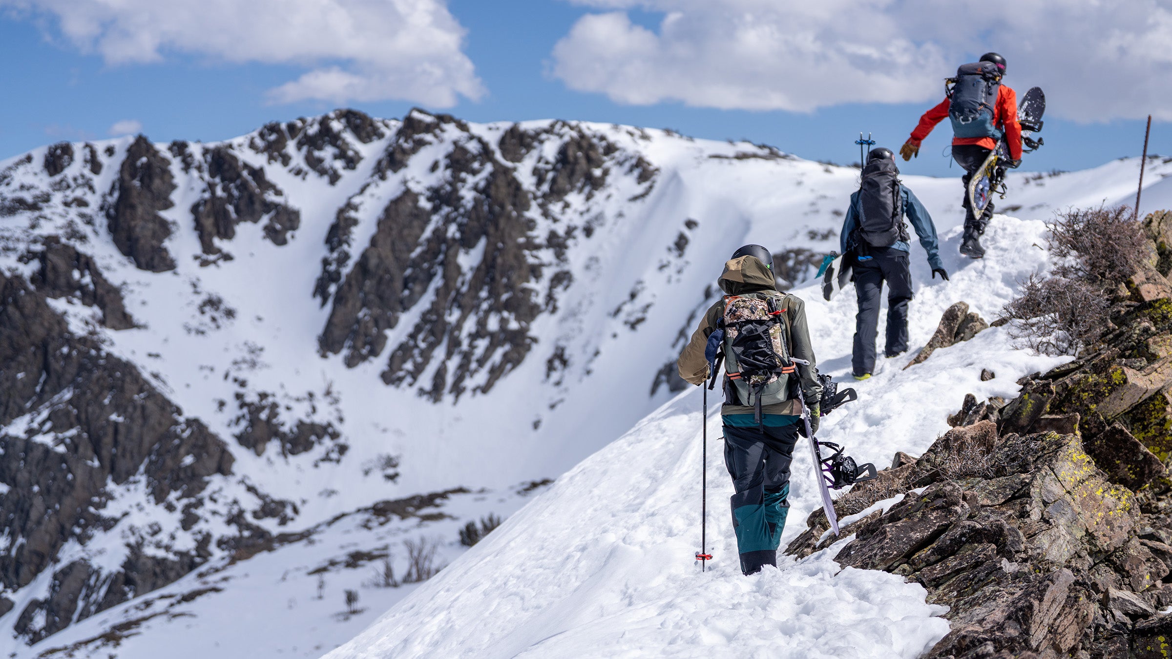 Snowboarders hiking snowy ridge towards mountain summit