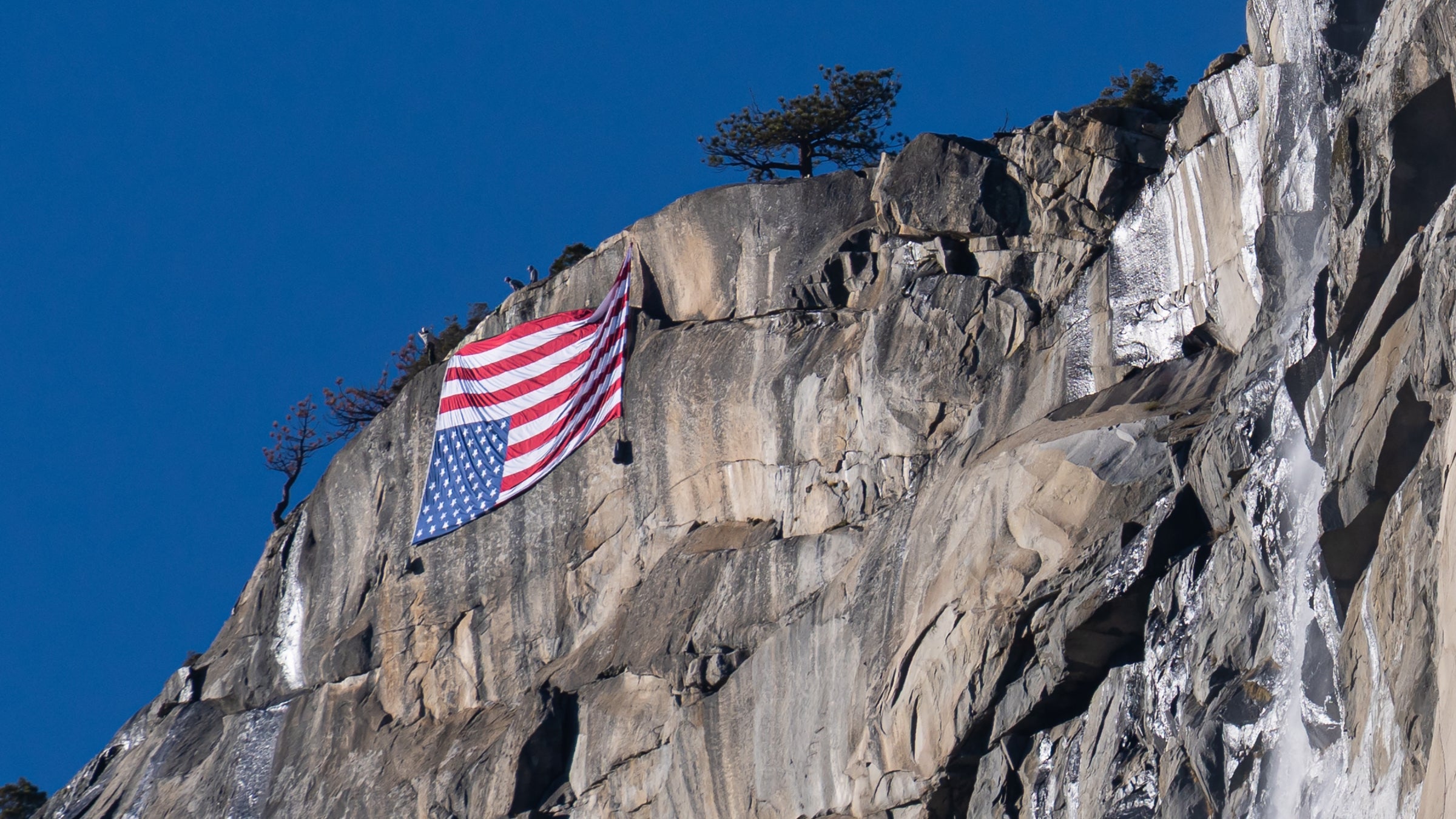 A large American flag hangs upside down on a cliff face.