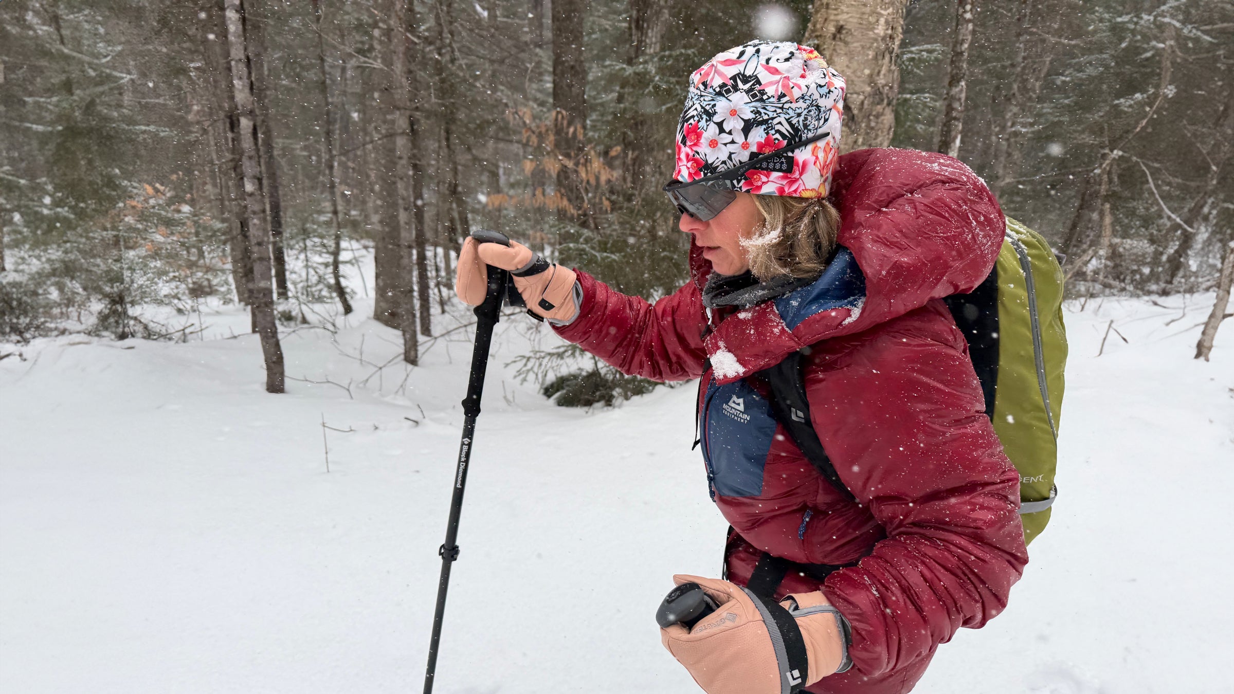 A winter cross-country skier moves through a snowy forest trail wearing the Mountain Equipment Oreus Hooded Jacket, a warm, weather-resistant synthetic jacket designed for active cold-weather adventures.